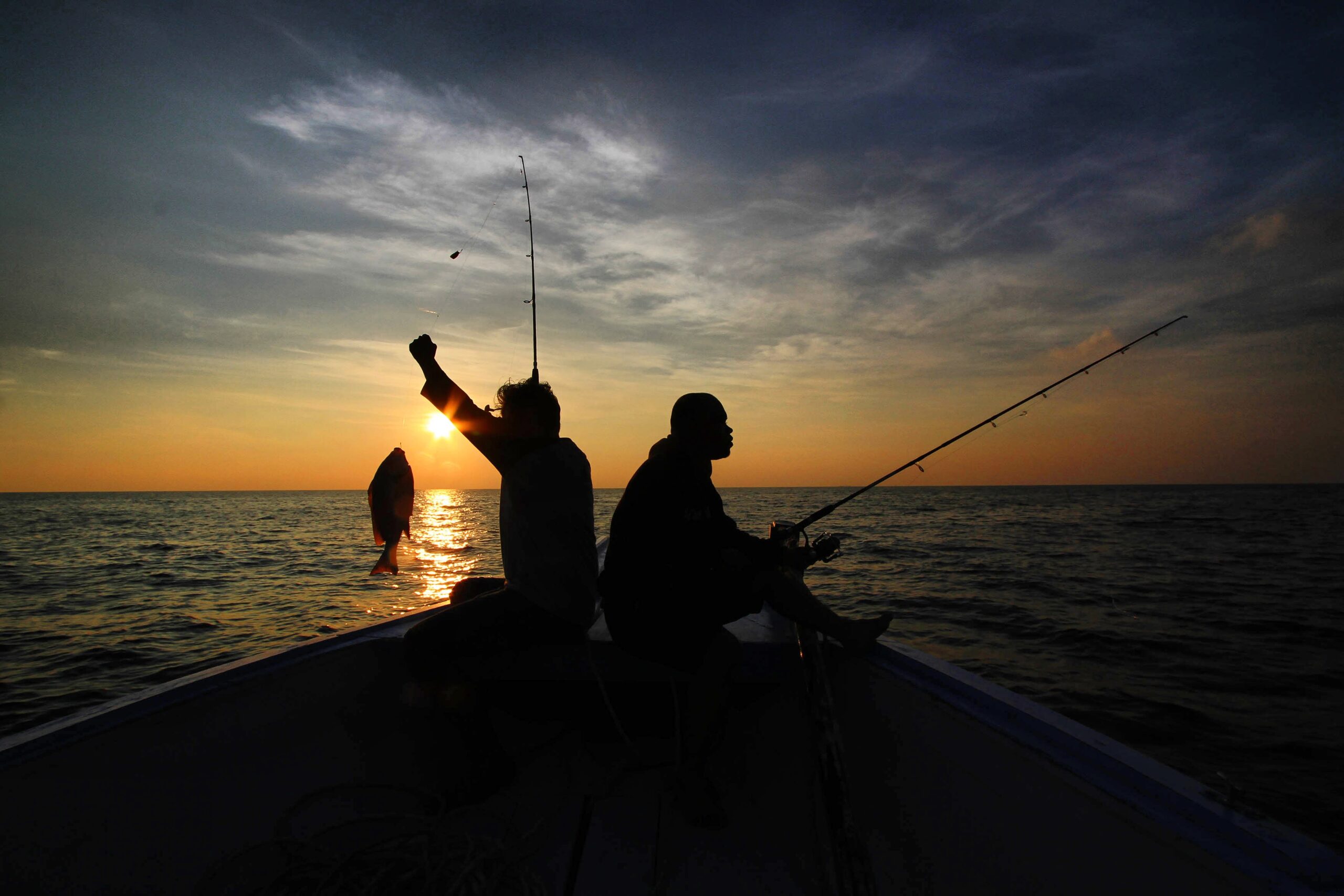 Silhouette Friends Fishing In Sea While Sitting On Boat Against Sky During Sunset